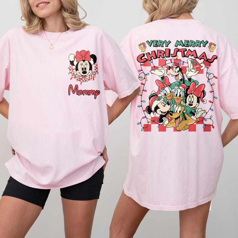 May include: Pink t-shirt featuring Minnie Mouse with a red bow and the word "Mommy". The back of the shirt displays a "Very Merry Christmas" design with Disney characters. The shirt has short sleeves.