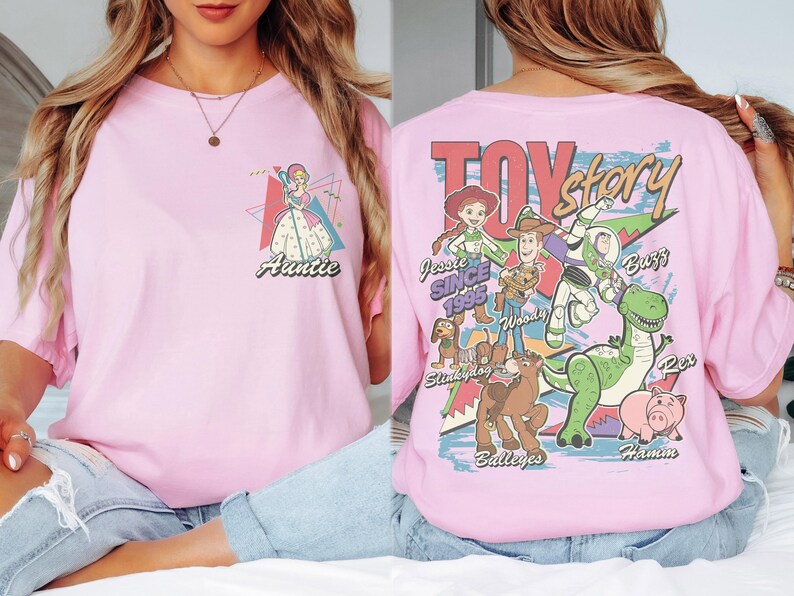 K&ouml;nnte beinhalten: Hellrosa T-Shirt mit einer Prinzessinnen-Grafik und dem Wort "Auntie" auf der Vorderseite. Auf der R&uuml;ckseite des Shirts stehen die Worte "Toy Story" und Charaktere wie Woody, Buzz und Rex.