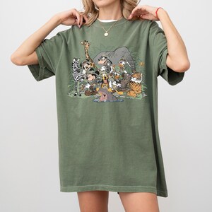 K&ouml;nnte beinhalten: Olivgr&uuml;nes T-Shirt mit einem Safari-Motiv. Das Design zeigt Zeichentricktiere wie Zebra, Giraffe, Elefant und Tiger sowie Micky Maus und Freunde, alle in Safari-Outfits.