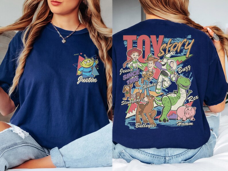 K&ouml;nnte beinhalten: Marineblaues T-Shirt mit einem Cartoon-Alien und dem Namen "Justin" auf der Vorderseite. Auf der R&uuml;ckseite befindet sich eine "Toy Story"-Grafik mit Figuren wie Woody, Buzz und Rex. Das Design enth&auml;lt den Text "Jessie Since 1995".