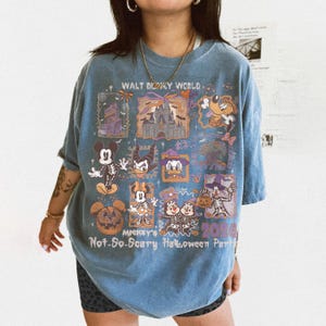 May include: Blue t-shirt featuring a colorful graphic design with the text "Walt Disney World" and "Mickey's Not-So-Scary Halloween Party 2026". The design includes various Disney characters in Halloween costumes.