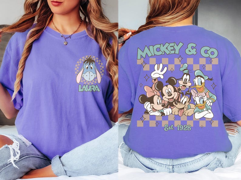 K&ouml;nnte beinhalten: Lilafarbenes T-Shirt mit einem Cartoon-Eeyore-Motiv und dem Namen "LAURA" auf der Vorderseite. Auf der R&uuml;ckseite ist eine Disney-Figurengruppe mit "MICKEY & CO" und "Est 1928" abgebildet.