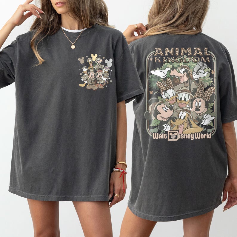 Puede incluir: Camiseta gris oscuro con un dise&ntilde;o de bolsillo con personajes de Disney. La parte trasera de la camiseta muestra un gr&aacute;fico m&aacute;s grande con el texto "ANIMAL KINGDOM" y "Walt Disney World". La camiseta tiene mangas cortas y un corte holgado.