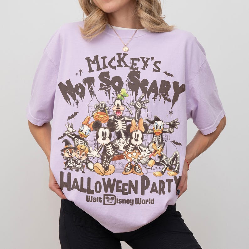 May include: A light purple t-shirt featuring a graphic of Disney characters in skeleton costumes. The text "Mickey's Not So Scary Halloween Party" and "Walt Disney World" are printed on the shirt.