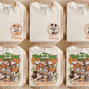 May include: Six off-white t-shirts. The top row features circular checkered patches with skeleton-costumed characters and text reading Mommy, Daddy, and Auntie. The bottom row displays a large graphic with Disney characters and Trick-or-Treat text.