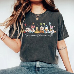 May include: Dark gray t-shirt featuring a colorful graphic of Disney characters, including Mickey and Minnie Mouse, Pluto, Goofy, Donald and Daisy Duck. The text "The happiest place on earth" is printed below the characters.