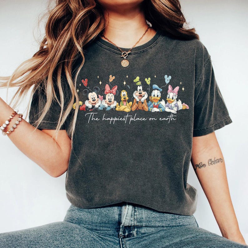 May include: Dark gray t-shirt featuring a colorful graphic of Disney characters, including Mickey and Minnie Mouse, Pluto, Goofy, Donald and Daisy Duck. The text "The happiest place on earth" is printed below the characters.