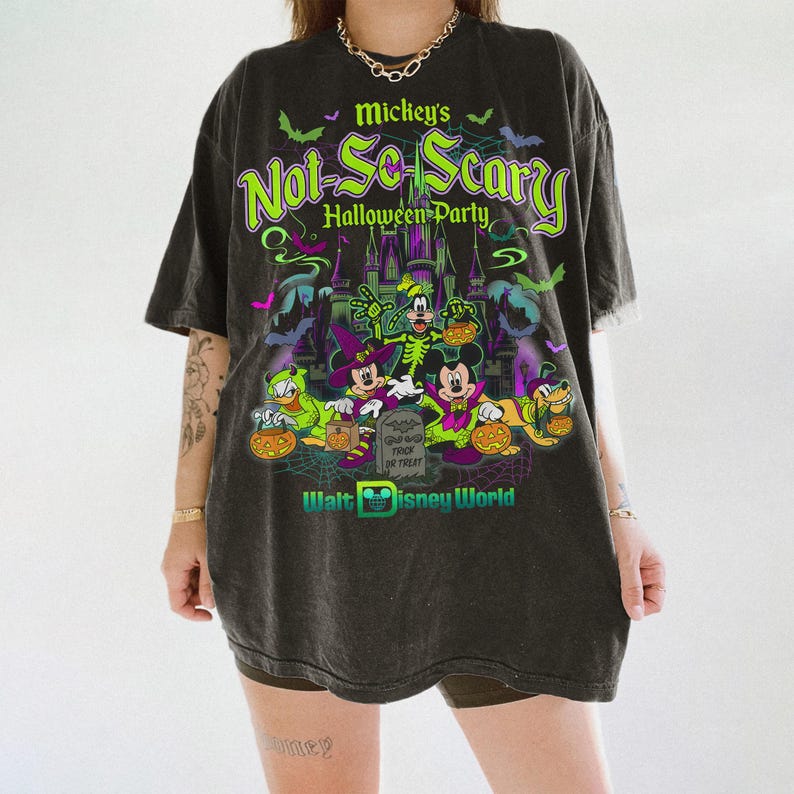 May include: A charcoal gray oversized t-shirt featuring a graphic print for Mickey's Not-So-Scary Halloween Party at Walt Disney World. The design includes Mickey, Minnie, Goofy, Donald, and Pluto in costumes, a castle, bats, and a tombstone.