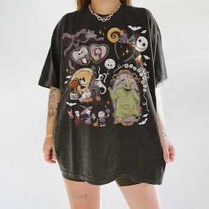 May include: Dark grey t-shirt with a colourful graphic from "The Nightmare Before Christmas." The design includes Jack Skellington, Sally, Oogie Boogie, and other characters. The shirt has a vintage, worn appearance.