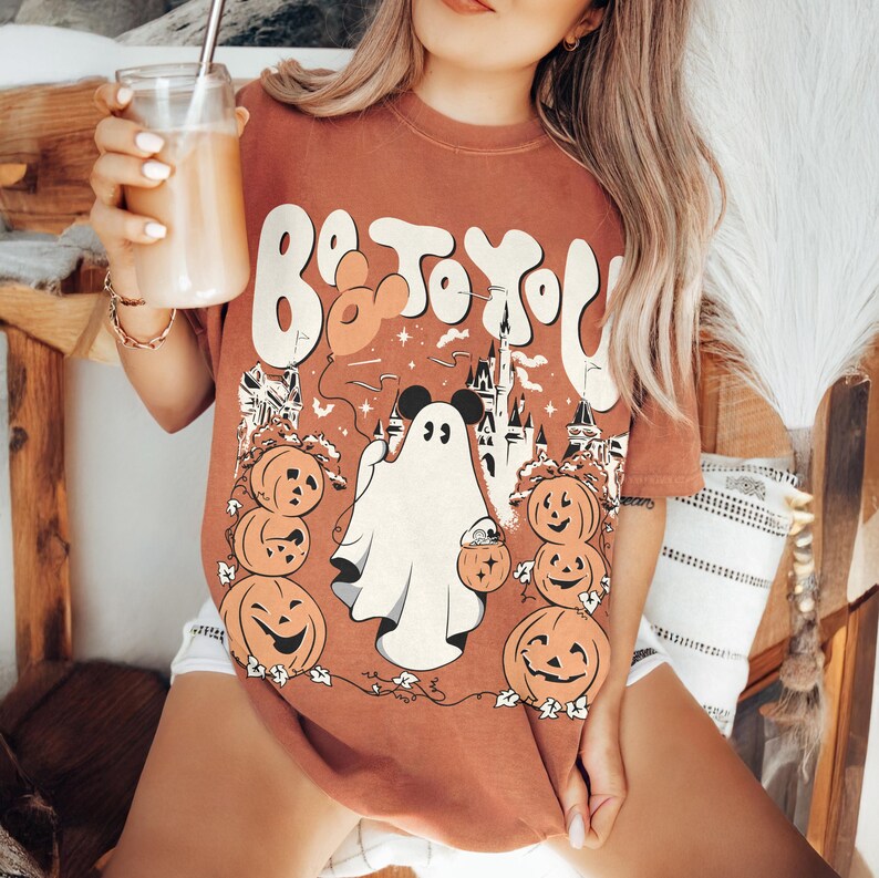 May include: A rust-coloured t-shirt with a Halloween graphic. The design includes a ghost, pumpkins, a castle, and the text "Boo To You". The graphic is in white, orange, and black.