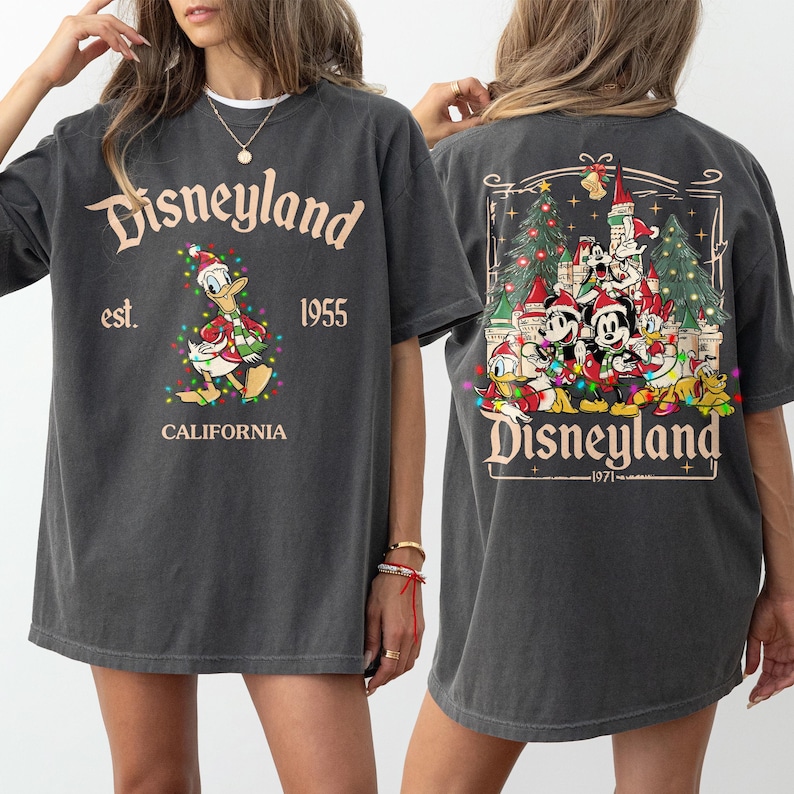 May include: Dark gray t-shirt with Disneyland graphics. The front features Donald Duck in a Santa hat and Christmas lights, with "Disneyland est. 1955 California" text. The back displays Disney characters in front of a castle and Christmas trees.