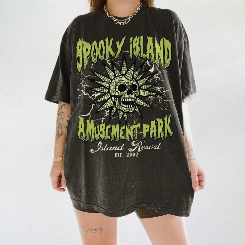 K&ouml;nnte beinhalten: Dunkelgraues T-Shirt mit einem Used-Look-Grafikdesign. Das Design zeigt einen Totenkopf mit Sonnenstrahlen, Blitzen und dem Text "Spooky Island Amusement Park Island Resort Est. 2002".
