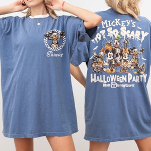 May include: Blue t-shirt with a white collar featuring a cartoon graphic on the front and back. The front graphic includes a character with the name "Gilbert". The back graphic says "Mickey's Not So Scary Halloween Party" with Disney characters in skeleton costumes.