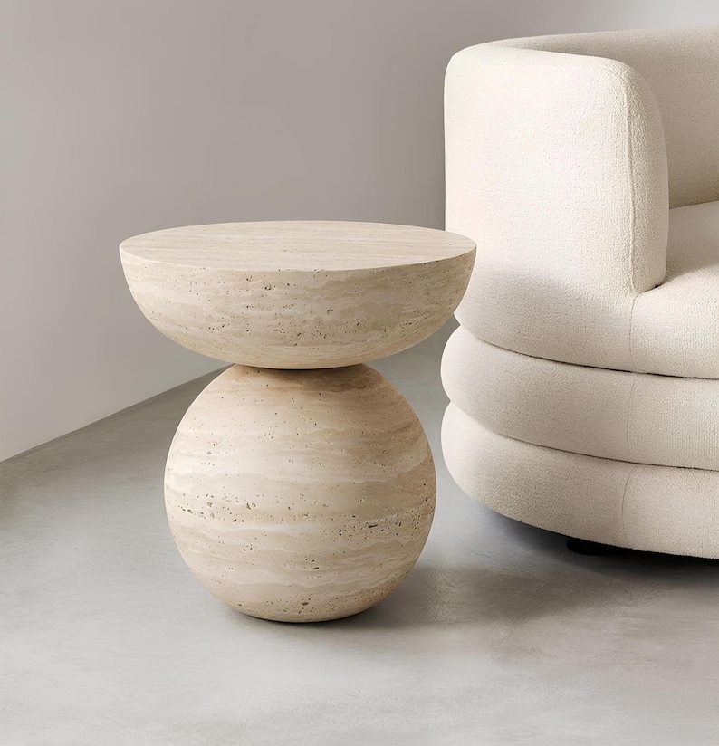 May include: A beige, modern side table with a unique hourglass shape. The table is made of a light-colored stone, with a round base and a flat, circular top. The table's height is approximately 18 inches.