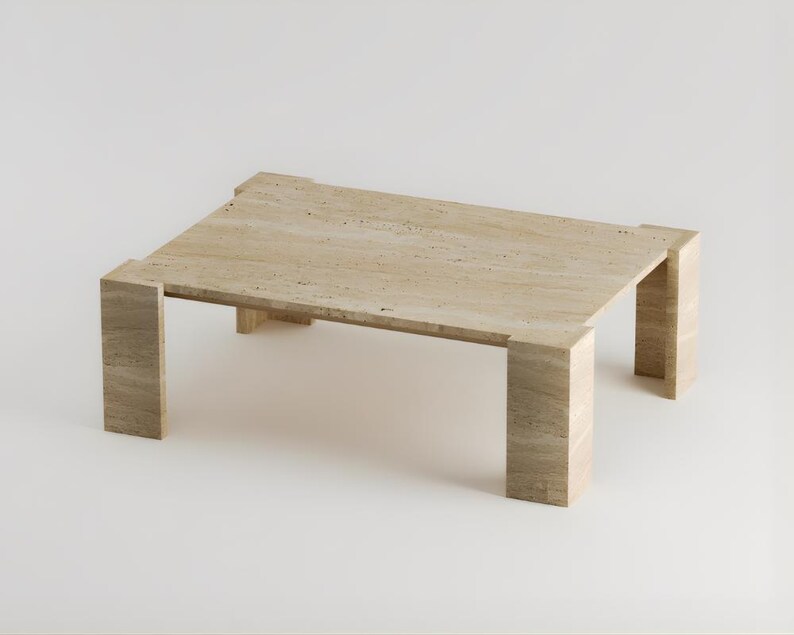 May include: A rectangular coffee table made of light beige stone. The table has a simple, modern design with a flat top and four thick, rectangular legs. The stone has a natural, textured appearance.