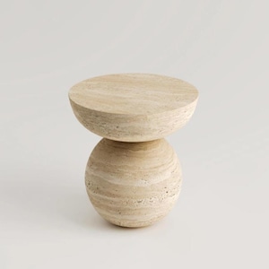 May include: A light beige, modern side table with a round top and a spherical base. The table is made of a stone-like material with a textured surface. The design is minimalist and contemporary.