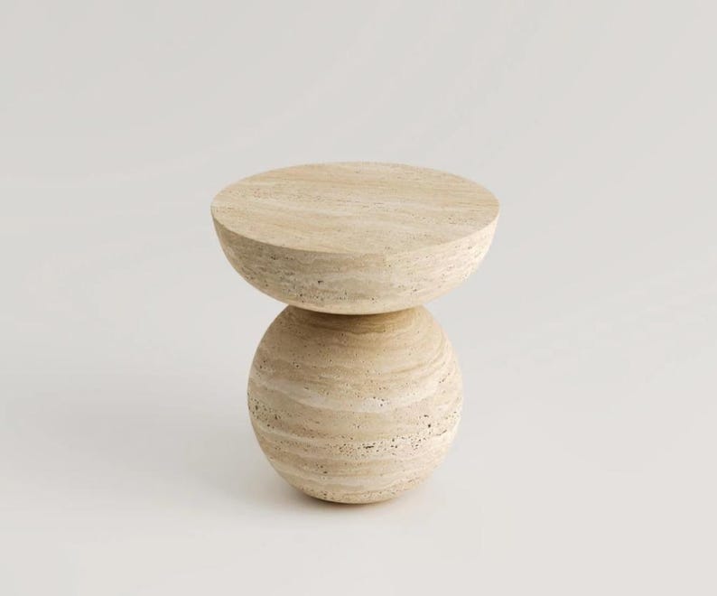 May include: A light beige, modern side table with a round top and a spherical base. The table is made of a stone-like material with a textured surface. The design is minimalist and contemporary.