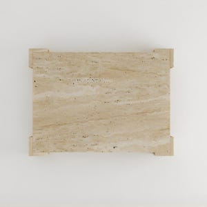May include: A rectangular travertine stone table with a light beige color and a natural, textured surface. The table has a simple design with four corner supports.