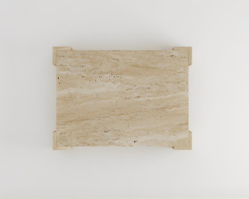 May include: A rectangular travertine stone table with a light beige color and a natural, textured surface. The table has a simple design with four corner supports.