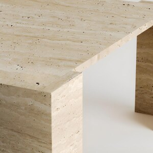 May include: A rectangular travertine table with a light beige color and dark speckles. The table has a minimalist design with a thick top and two supporting legs. The table's dimensions are approximately 60 inches long, 30 inches wide, and 16 inches high.