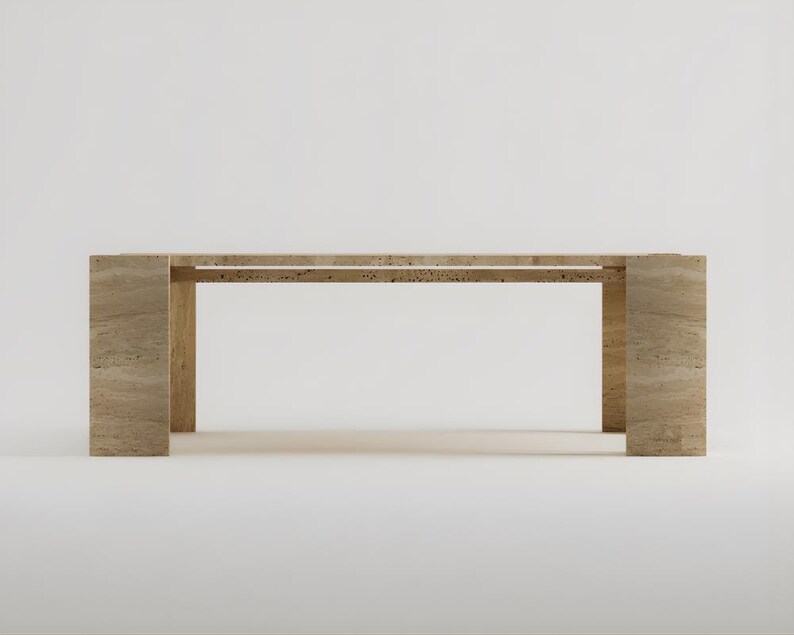 May include: A rectangular, light-colored stone table with a minimalist design. The table has a long, flat top supported by two thick, rectangular legs at each end. The table is approximately 72 inches long.