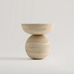 May include: A beige, modern side table with a rounded base and a half-circle top. The table is made of a stone-like material and has a natural, textured appearance. The design is minimalist and sculptural, suitable for a living room or bedroom.