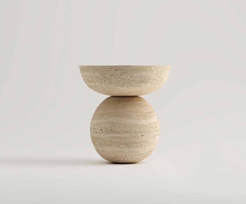 May include: A beige, modern side table with a rounded base and a half-circle top. The table is made of a stone-like material and has a natural, textured appearance. The design is minimalist and sculptural, suitable for a living room or bedroom.