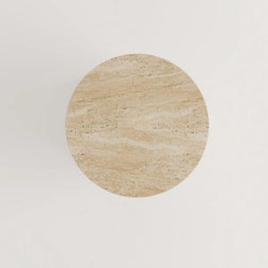 May include: Overhead view of a round, beige travertine stone table. The table has a natural, textured surface with subtle variations in color and pattern. The table is set against a white background.