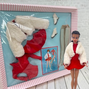 May include: A vintage doll wearing a red dress and white faux fur jacket, displayed next to a boxed set containing a matching red dress, white faux fur jacket, white ice skates, and beige tights, with an illustration of the outfit included.