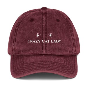 May include: A maroon vintage-style baseball cap with white embroidered text that reads "CRAZY CAT LADY" and two white cat ears above the text.