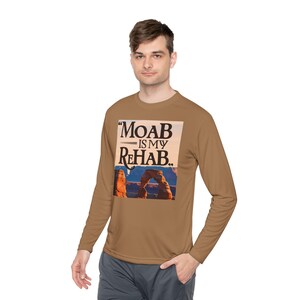 May include: A brown long-sleeve shirt with a graphic print of a red rock arch and the text "MOAB IS MY REHAB."