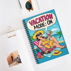 Puede incluir: Una libreta espiral azul con una ilustración de dibujos animados de una mujer con gafas de sol y un sombrero, relajándose en una silla de playa con un cóctel. El texto "Vacation Mode: On" está en un bocadillo de diálogo sobre su cabeza.