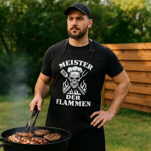 Peut inclure: Un tablier noir avec le texte "MEISTER DER FLAMMEN" et un motif de crâne, porté par une personne faisant un barbecue. La personne porte un t-shirt noir et une casquette noire. Le grill contient des hamburgers et des légumes cuits.