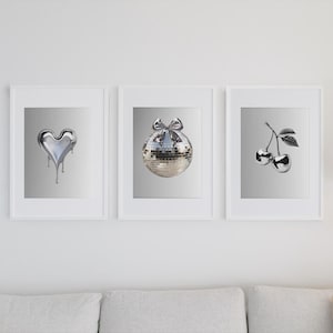 May include: Three framed prints with silver metallic designs. The left print features a heart shape, the middle print features a disco ball, and the right print features two cherries.