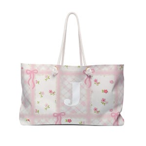 May include: A white tote bag with pink and white checkered pattern and pink floral accents. The bag has white rope handles and a white letter "J" in the center.