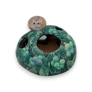 May include: A ceramic incense burner with a green and blue design featuring leaves and berries. A small painted cat sits on top of the burner.