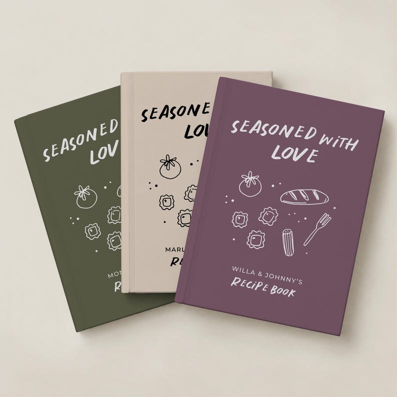 May include: Three hardcover recipe books in olive green, beige, and plum purple. Each cover features the white text "SEASONED WITH LOVE" and line art illustrations of food items like tomatoes, pasta, bread, and a fork.