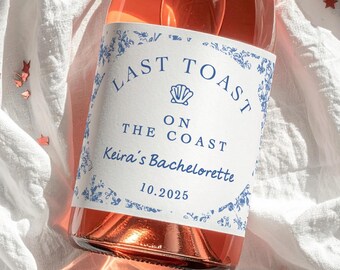 May include: A bottle of rosé wine with a custom label. The label reads "LAST TOAST ON THE COAST Keira's Bachelorette 10.2025" in blue text with a seashell graphic and floral border. The bottle is partially visible.