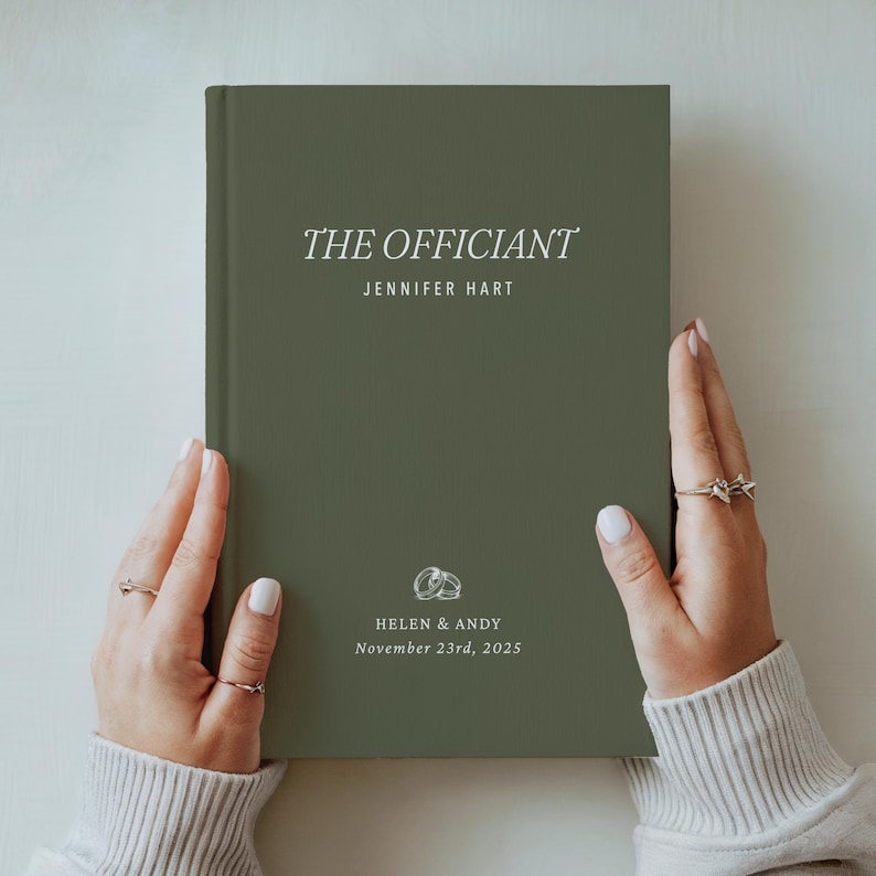 May include: An olive green book with the title "THE OFFICIANT" in white script. The name "JENNIFER HART" is below the title. The bottom of the book has the names "HELEN & ANDY" and the date "November 23rd, 2025".