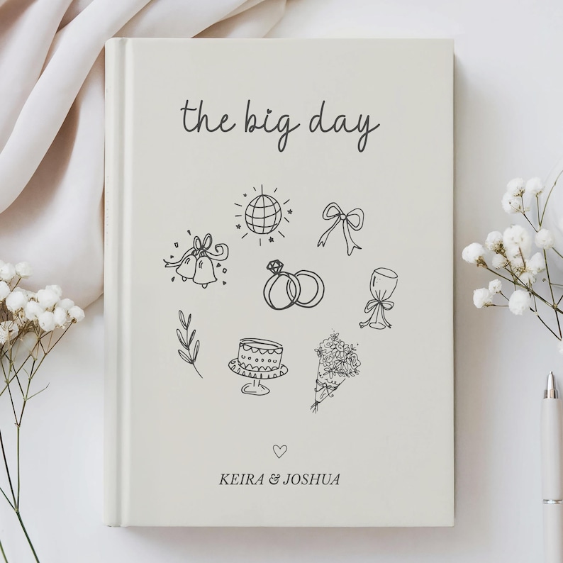 Pu&ograve; includere: Diario di nozze color crema con la scritta "the big day". La copertina presenta disegni a tratto nero di icone nuziali, tra cui anelli, campane e una torta. I nomi "Keira & Joshua" sono stampati sotto.