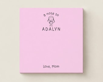 May include: A square light pink notepad featuring a black line drawing of a person with pigtails. The text reads a note to ADALYN at the top and Love, Mom at the bottom. The design is centered on the paper with ample space for writing notes.