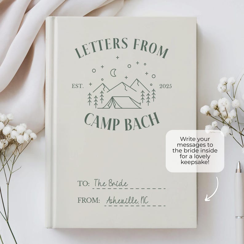 Puede incluir: Un libro blanco con un logotipo verde que dice "Letters From Camp Bach Est. 2025". El libro tiene una l&iacute;nea para "To: The Bride" y "From: Asheville, NC". El libro est&aacute; sobre una superficie blanca con flores blancas.