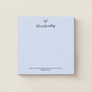 May include: A square light blue notepad featuring a small black heart icon above the cursive text "olivia's notes" at the top. At the bottom, the text "GOD IS WITHIN HER, SHE WILL NOT FALL. PSALM 46:5" is printed in a clean black sans-serif font.