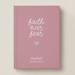 May include: A dusty rose hardcover journal featuring white cursive text that reads faith over fear with a small heart icon below it. The bottom of the cover displays the name Kayley's followed by the words PRAYER JOURNAL in white capital letters.