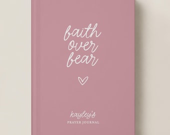 May include: A dusty rose hardcover journal featuring white cursive text that reads faith over fear with a small heart icon below it. The bottom of the cover displays the name Kayley's followed by the words PRAYER JOURNAL in white capital letters.