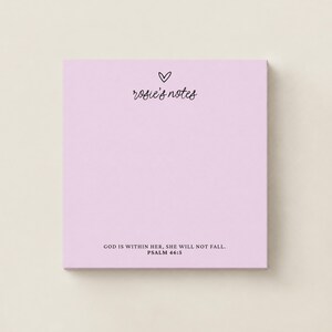 May include: A square light purple notepad featuring a small black heart icon above the text "rosie's notes" in a cursive font. At the bottom, the text "GOD IS WITHIN HER, SHE WILL NOT FALL. PSALM 46:5" is printed in a clean, black sans-serif font.