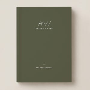 May include: A dark olive green hardcover book with white text on the front cover. The text reads K+N, KAYLEY + NATE, and our love letters. The design features a minimalist layout with a thin horizontal line above the final phrase.