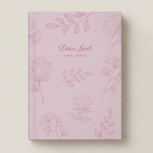 May include: A light pink hardcover journal featuring a delicate, dark pink line-art floral pattern across the cover. The text "Dear God" is printed in a script font above the words "LOVE, GRACE" in a simple, clean sans-serif typeface.