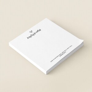 May include: A square stack of white paper sheets featuring the black printed text 'kayley's notes' with a small heart icon above it, and the text 'GOD IS WITHIN HER, SHE WILL NOT FALL. PSALM 46:5' printed in the bottom right corner.