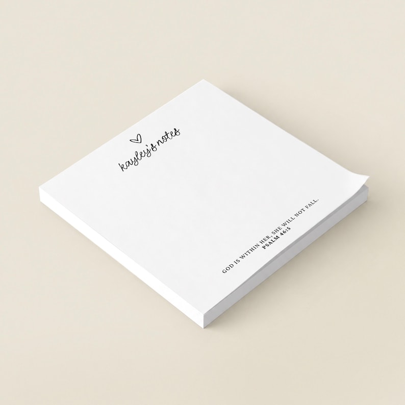 May include: A square stack of white paper sheets featuring the black printed text 'kayley's notes' with a small heart icon above it, and the text 'GOD IS WITHIN HER, SHE WILL NOT FALL. PSALM 46:5' printed in the bottom right corner.